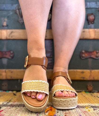 Brown sandals with beige straps worn by a person on a textured surface.
