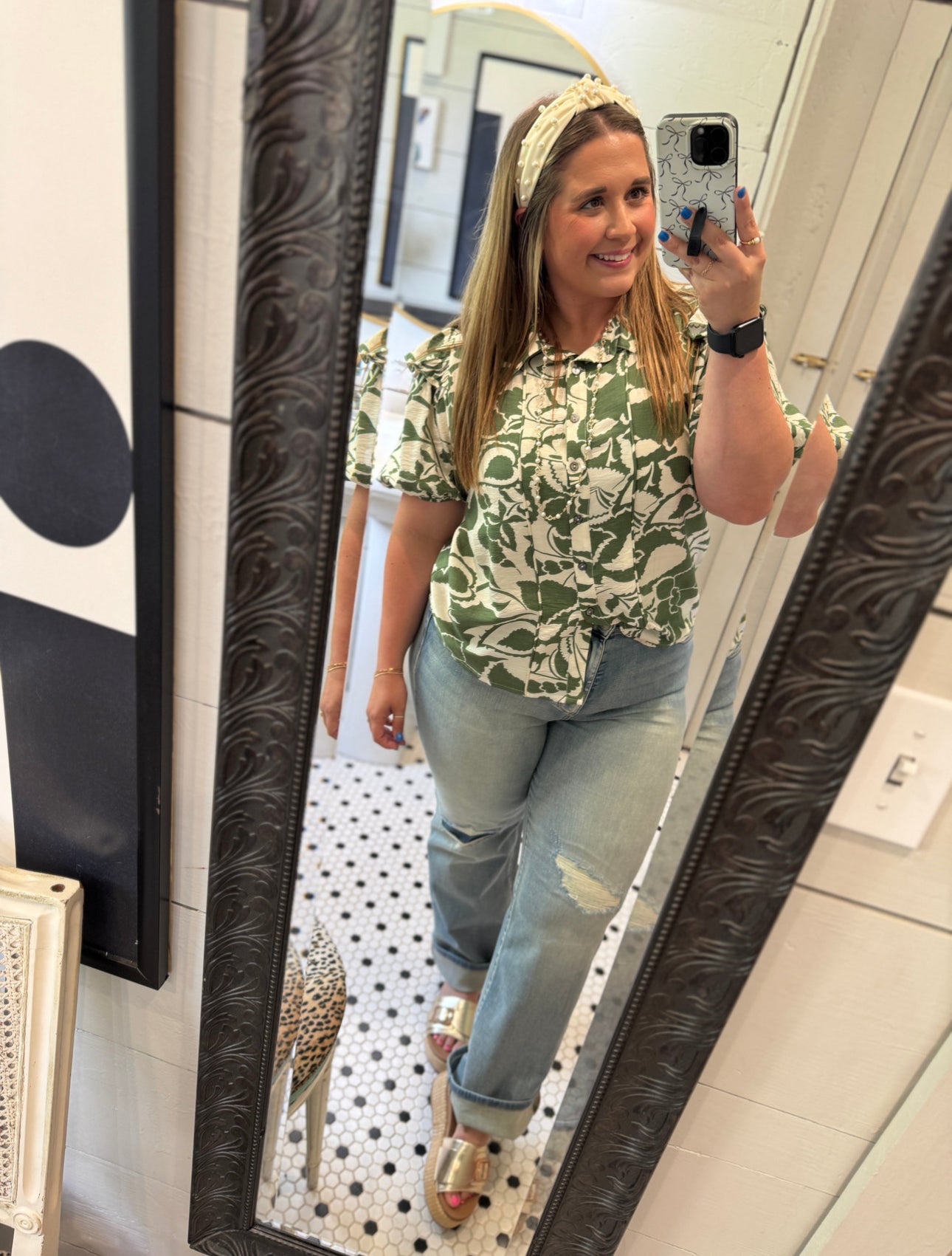 Woman taking a mirror selfie wearing a green patterned shirt and jeans.