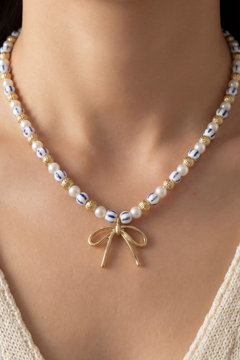 Pearl necklace with a gold bow pendant on a person wearing a beige top.
