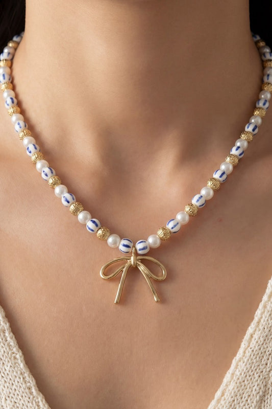 Pearl necklace with a gold bow pendant on a person wearing a beige top.