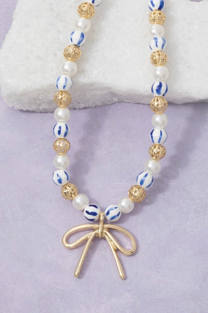Necklace with beads and a gold bow charm on a light purple background