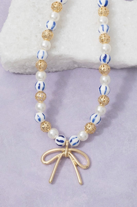Necklace with beads and a gold bow charm on a light purple background