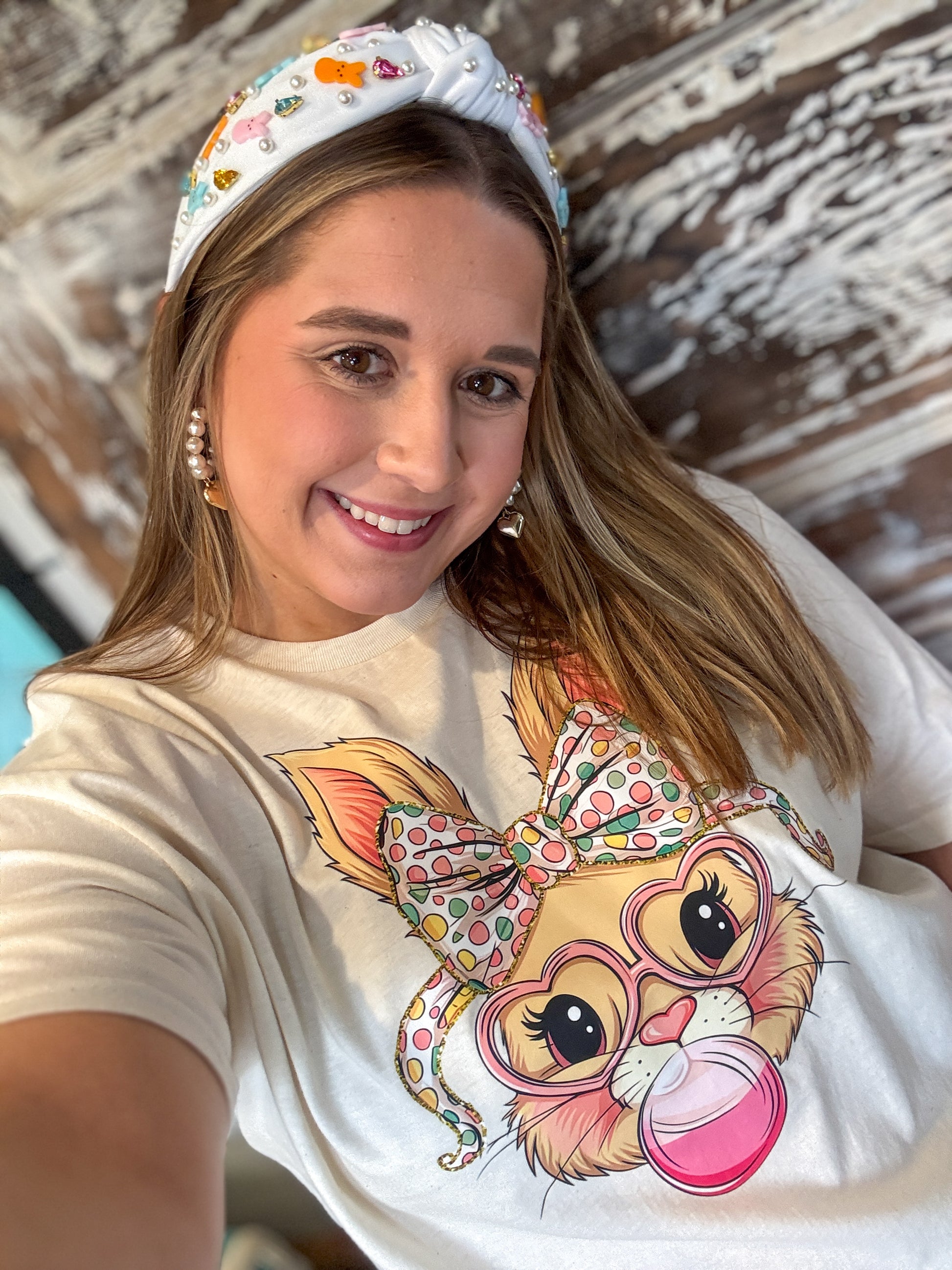 Woman wearing a t-shirt with a cartoon character design, smiling in front of a wooden wall.