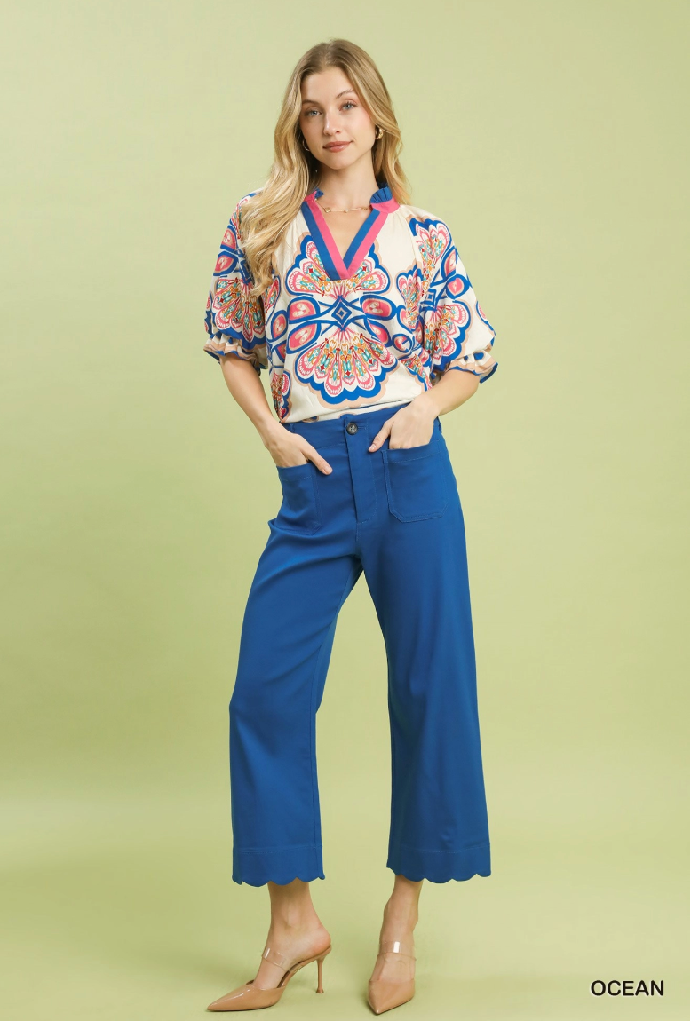 Woman wearing a patterned blouse and blue pants on a light green background