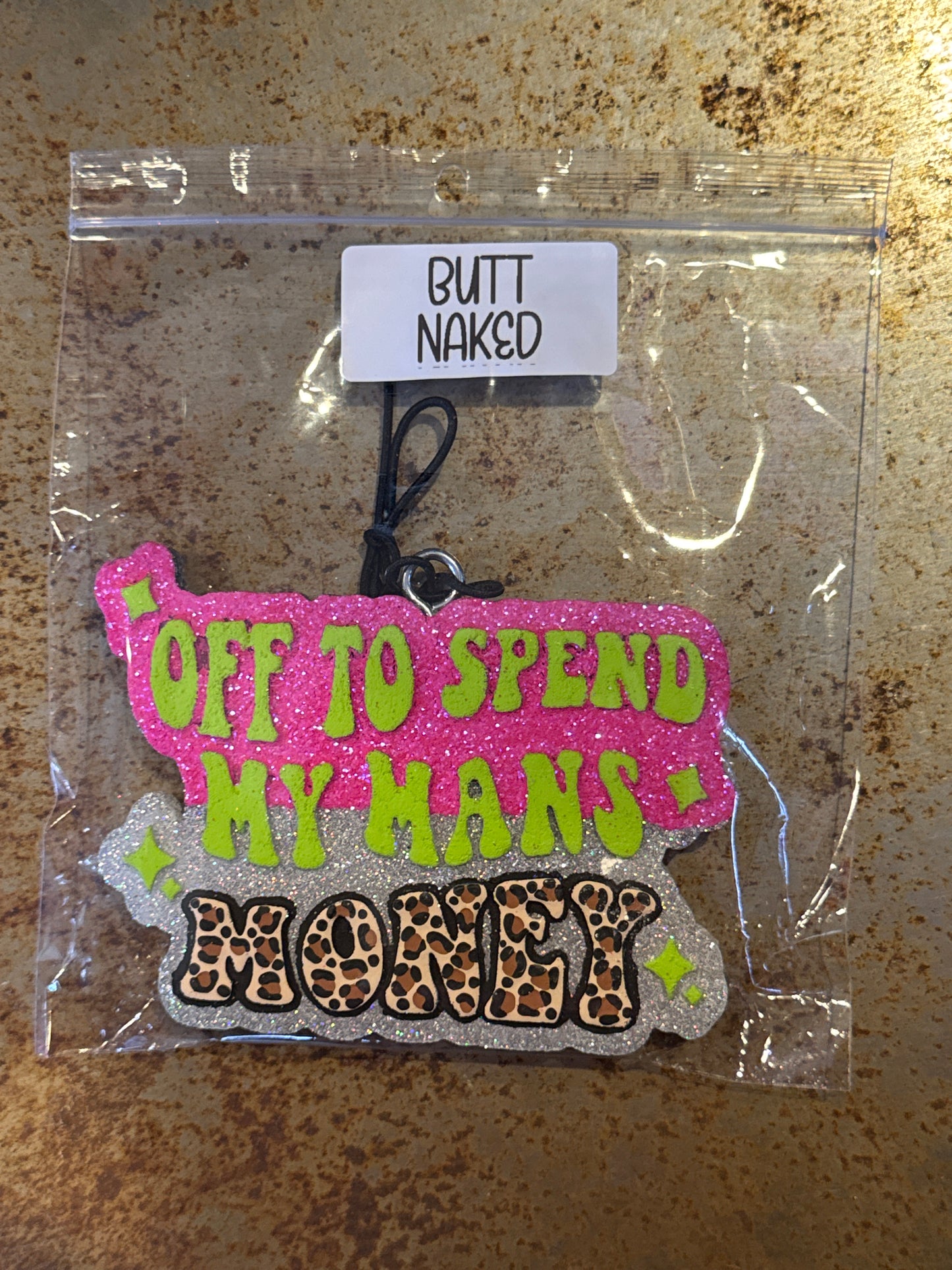 Keychain with text and leopard print design in clear packaging on a rusty surface