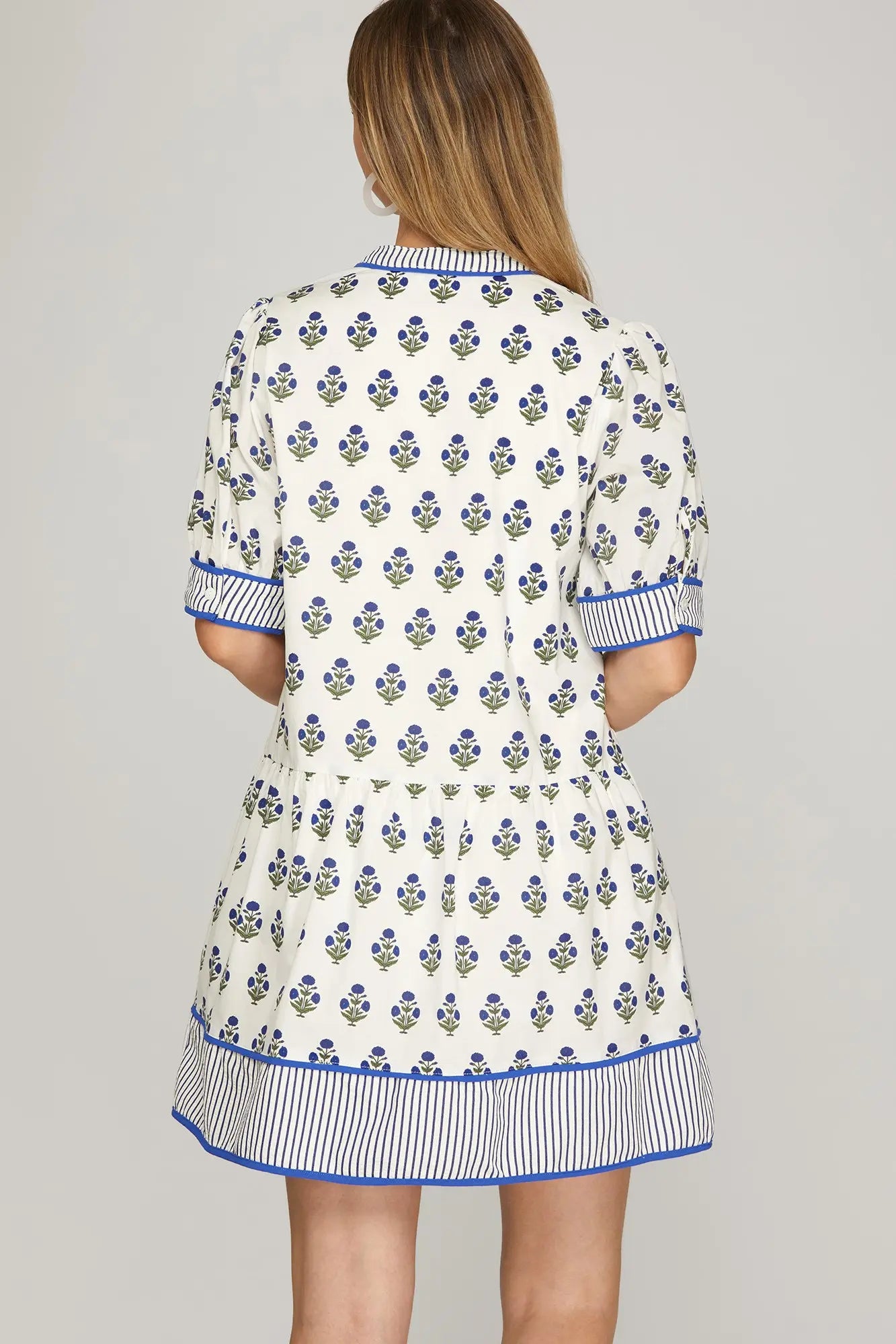 Woman wearing a white dress with blue floral pattern on a gray background