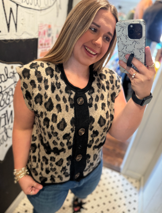Woman taking a mirror selfie wearing a leopard print top and blue jeans.