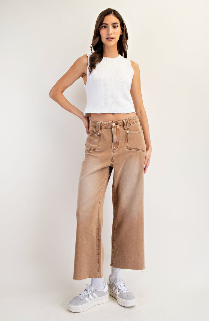 Woman wearing a white sleeveless top and beige high-waisted jeans on a white background