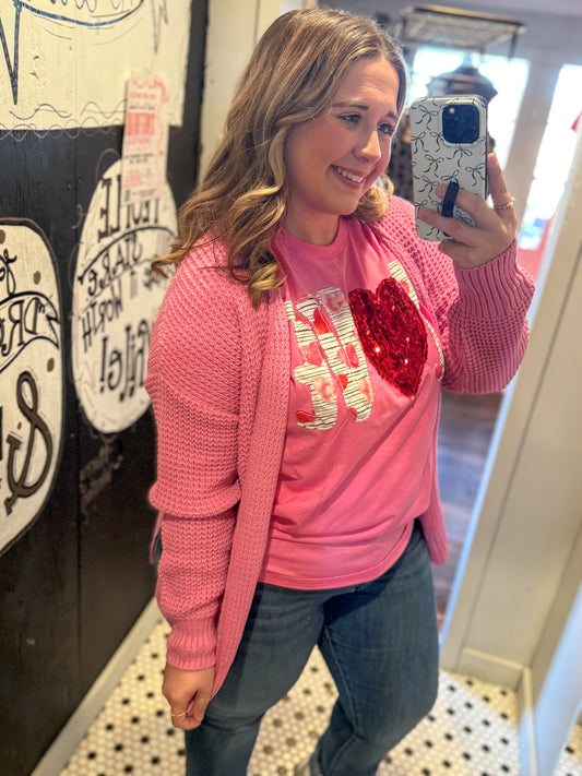 Woman taking a mirror selfie wearing a pink sweater with a heart design.
