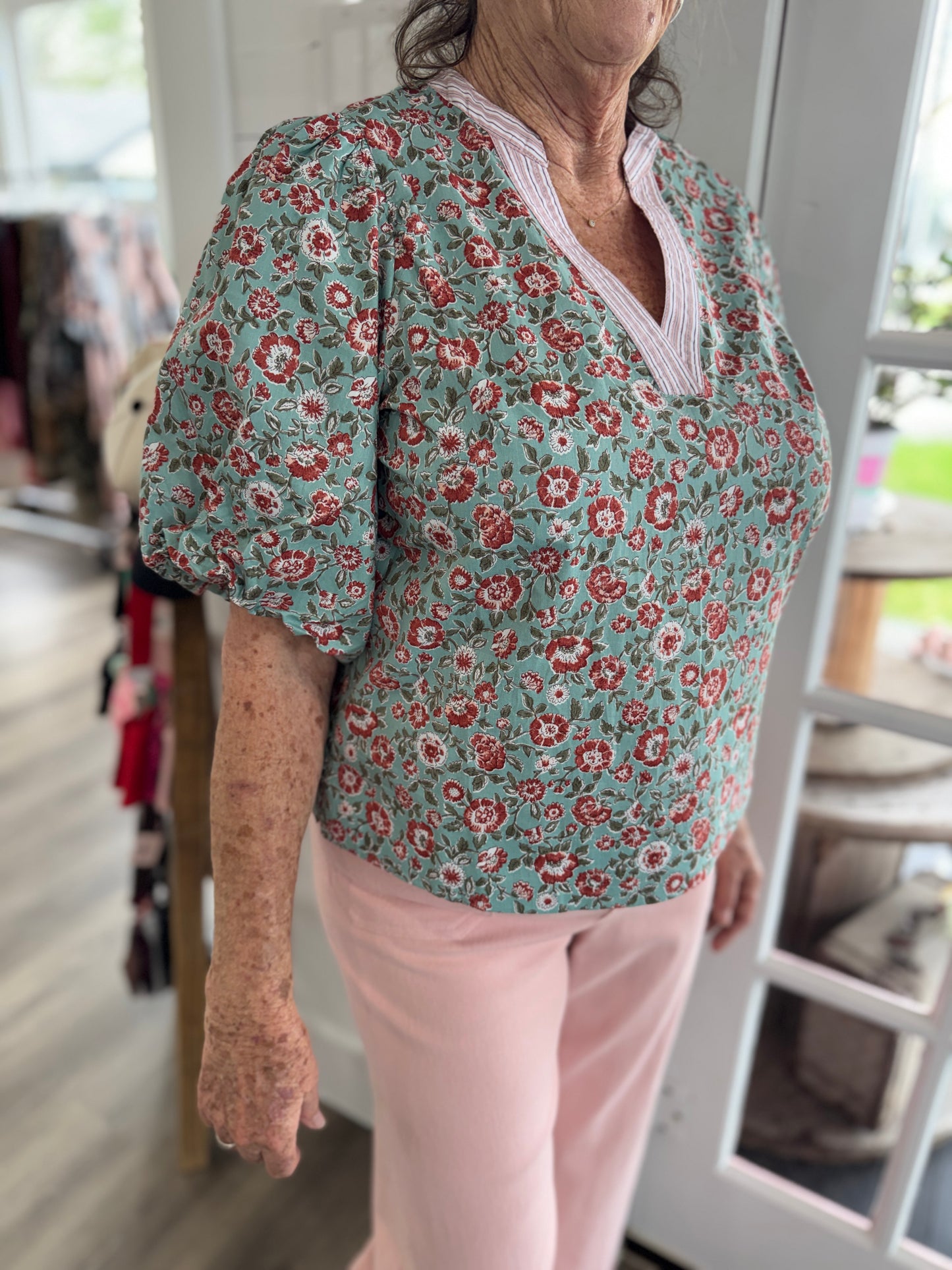 Person wearing a floral blouse with puffed sleeves and pink pants in an indoor setting.