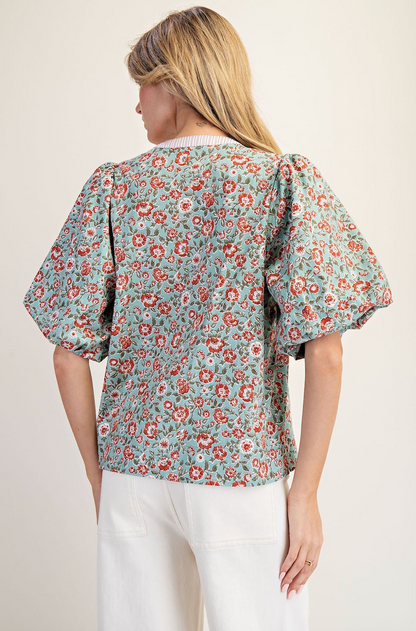 Woman wearing a floral blouse with puff sleeves on a plain background