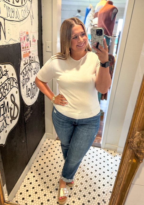 Woman taking a mirror selfie wearing a white t-shirt and blue jeans in a store.