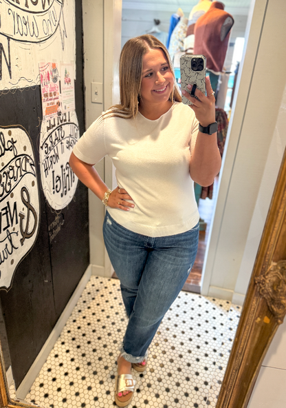 Woman taking a mirror selfie wearing a white t-shirt and blue jeans in a store.