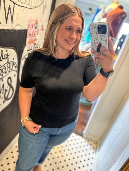 Woman taking a mirror selfie wearing a black t-shirt and blue jeans indoors.