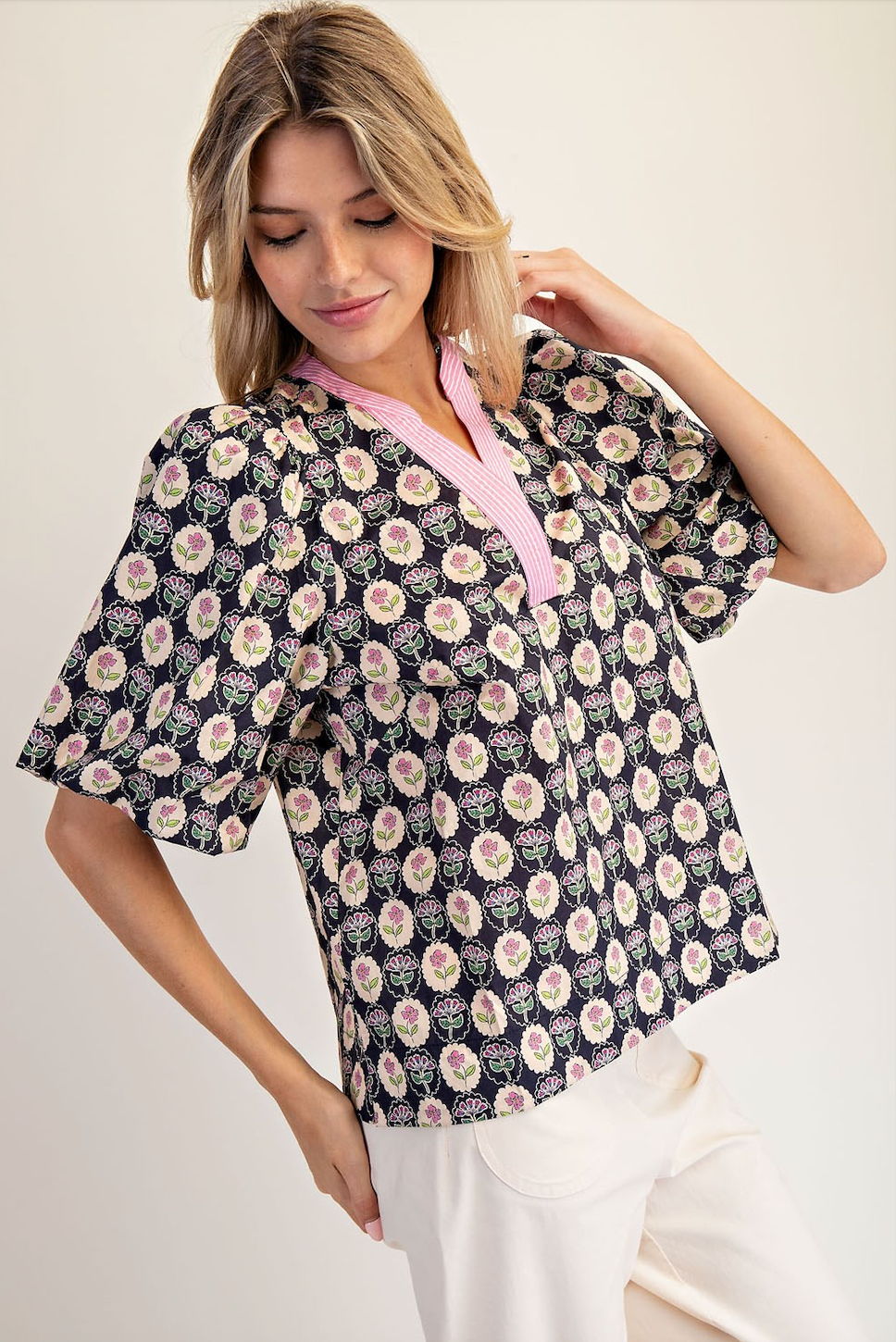 Woman wearing a floral patterned blouse with a pink collar against a white background