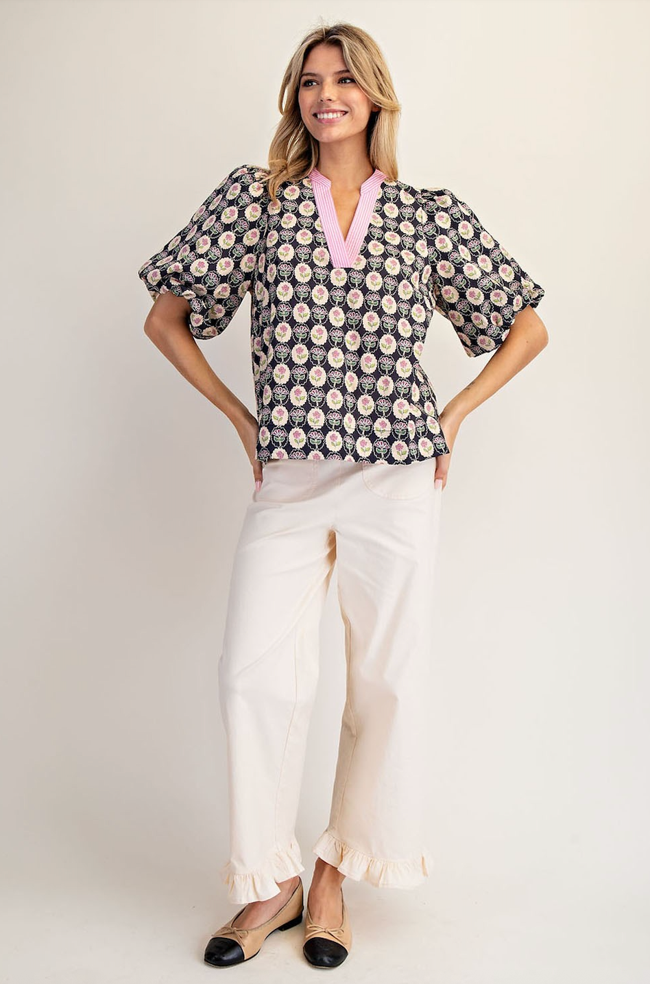 Woman wearing a patterned blouse and white pants on a plain background