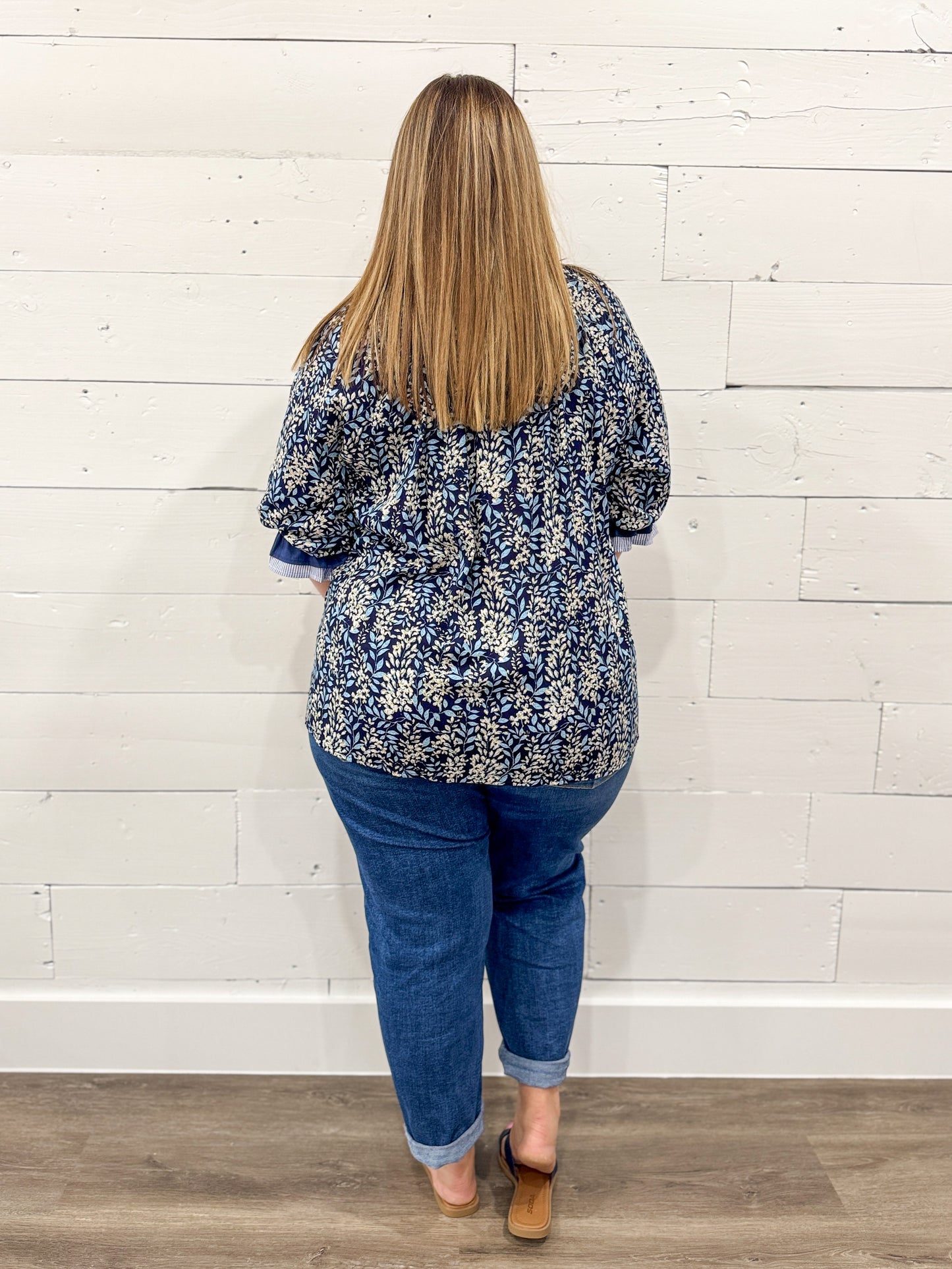 Woman wearing a blue floral blouse and jeans against a white wooden panel background