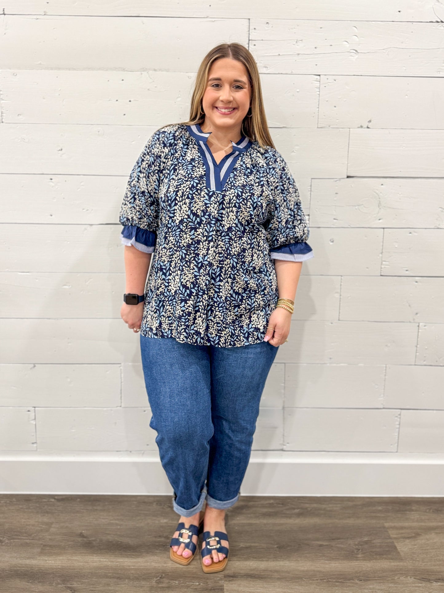 Woman wearing a blue floral blouse and jeans against a white wooden panel background