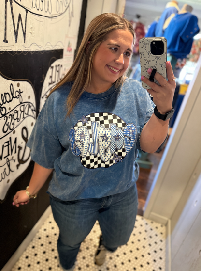 Woman taking a mirror selfie wearing a blue graphic t-shirt in a store.