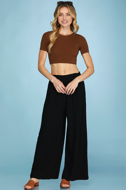 Woman wearing a brown crop top and black wide-leg pants on a light blue background
