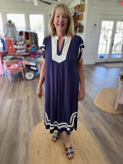 Woman in a blue dress standing in a room with wooden flooring and furniture.