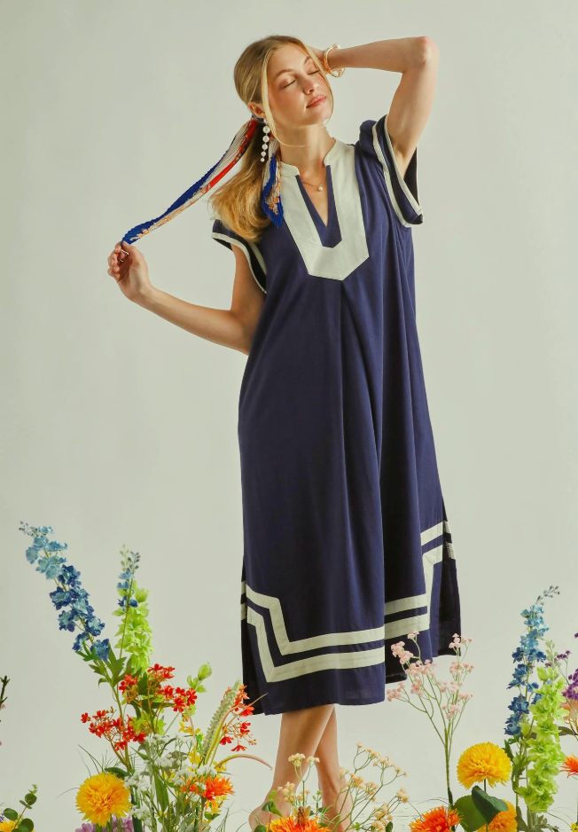 Woman wearing a navy dress with white trim standing among flowers on a light background