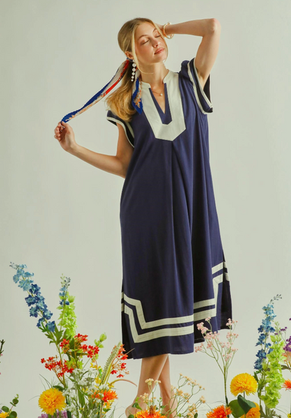 Woman wearing a navy dress with white trim standing among flowers on a light background