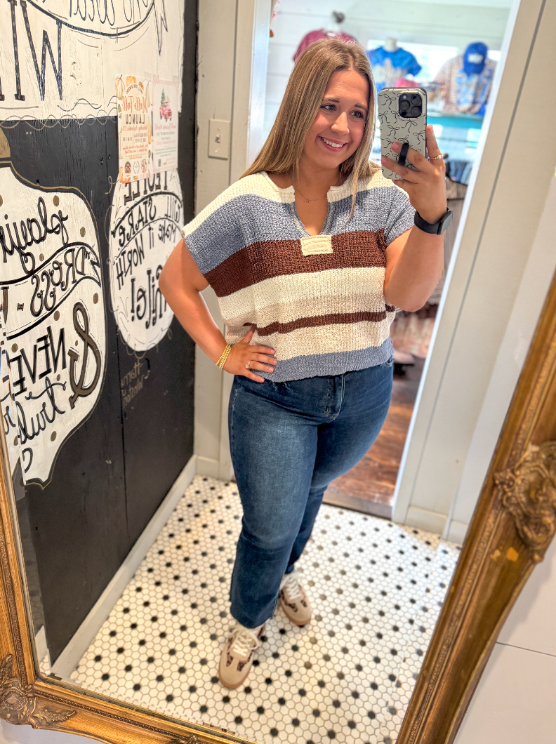 Woman taking a mirror selfie wearing a striped shirt and jeans in a room with decorative elements.