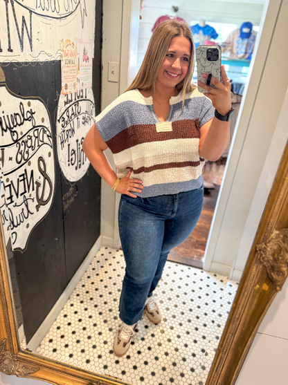 Woman taking a mirror selfie wearing a striped shirt and jeans in a room with decorative elements.