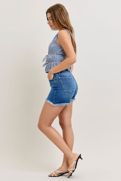 Woman wearing a checkered top and denim shorts on a plain background