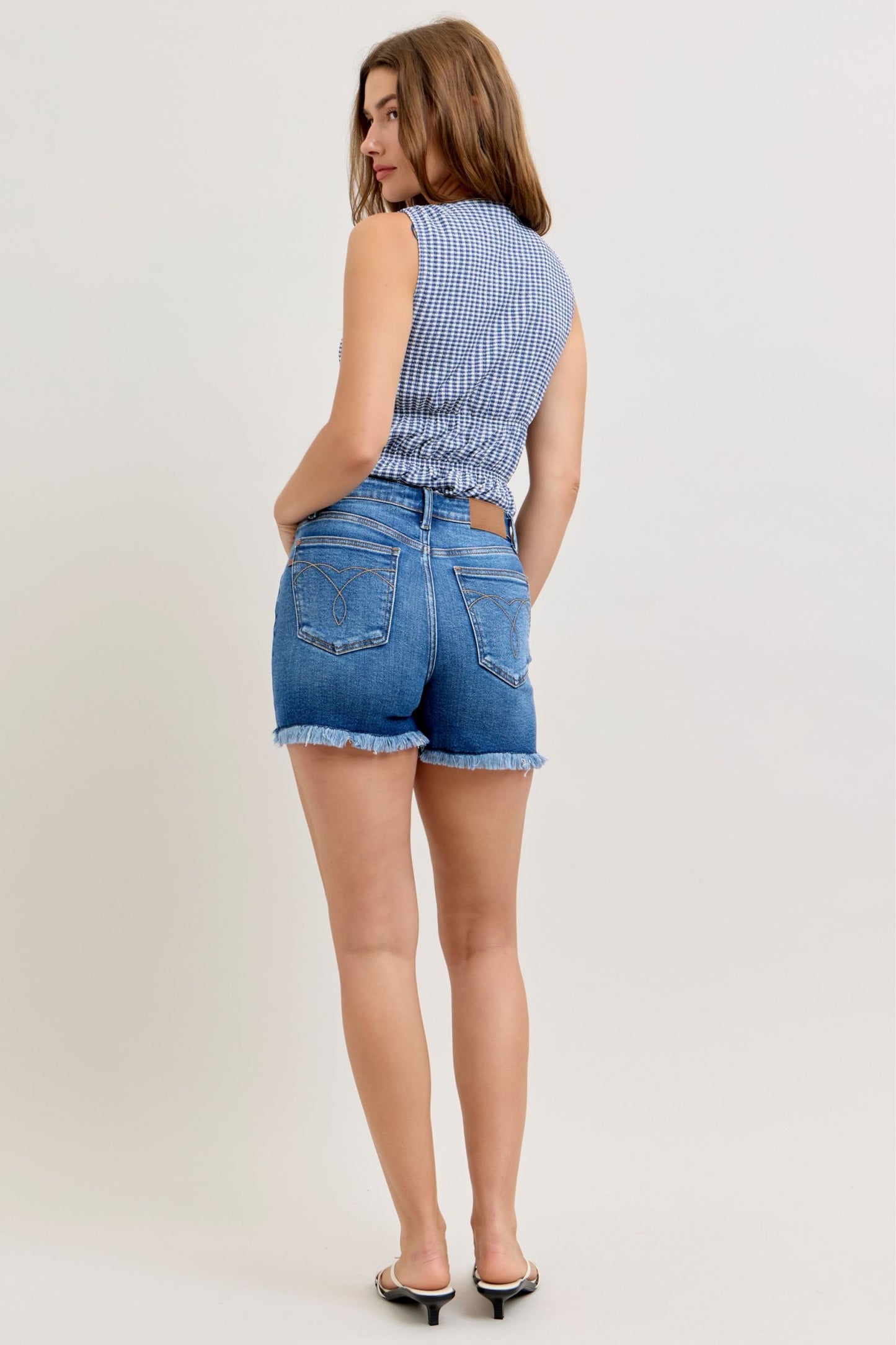 Woman wearing a blue checkered top and denim shorts on a white background