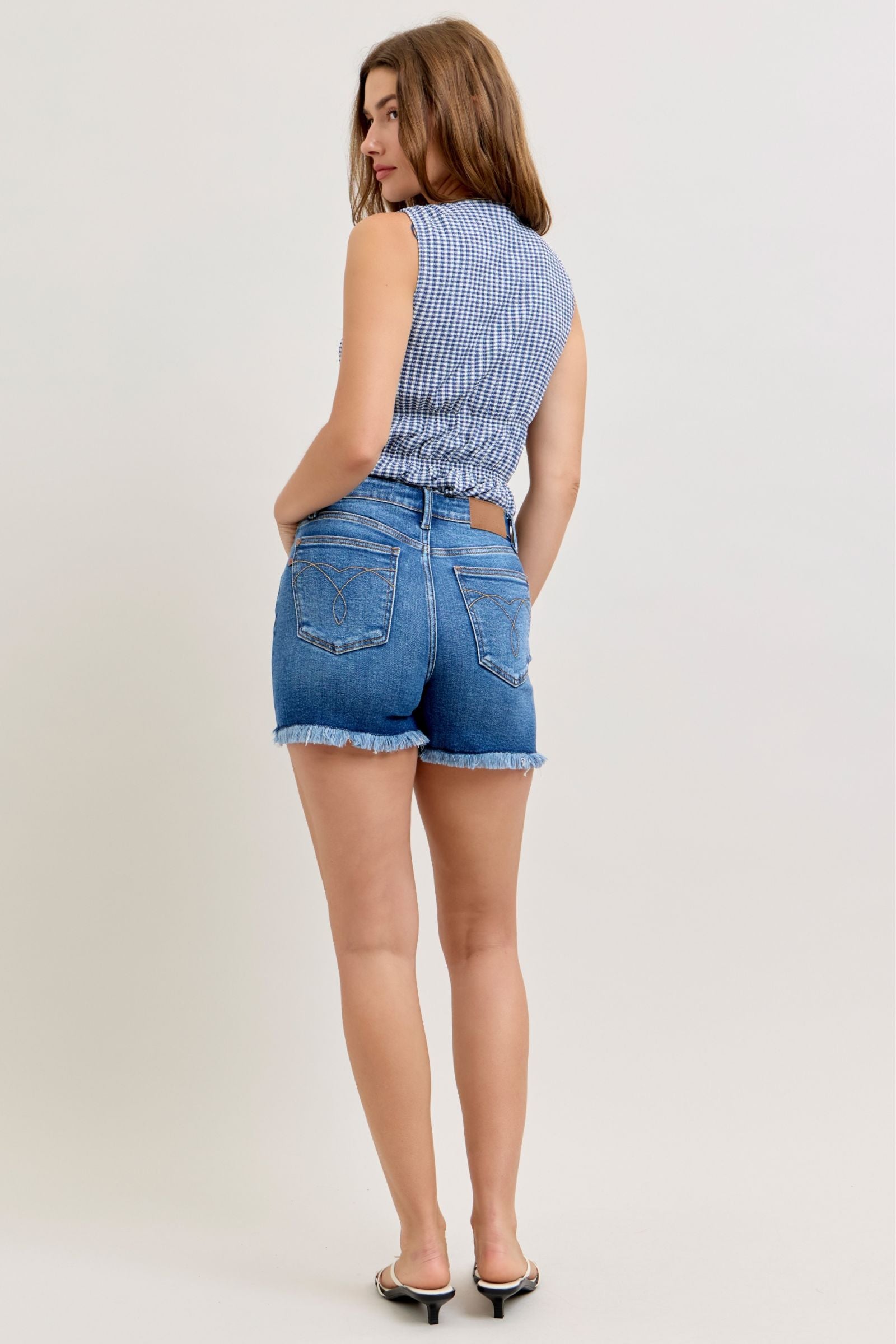 Woman wearing a blue checkered top and denim shorts on a white background
