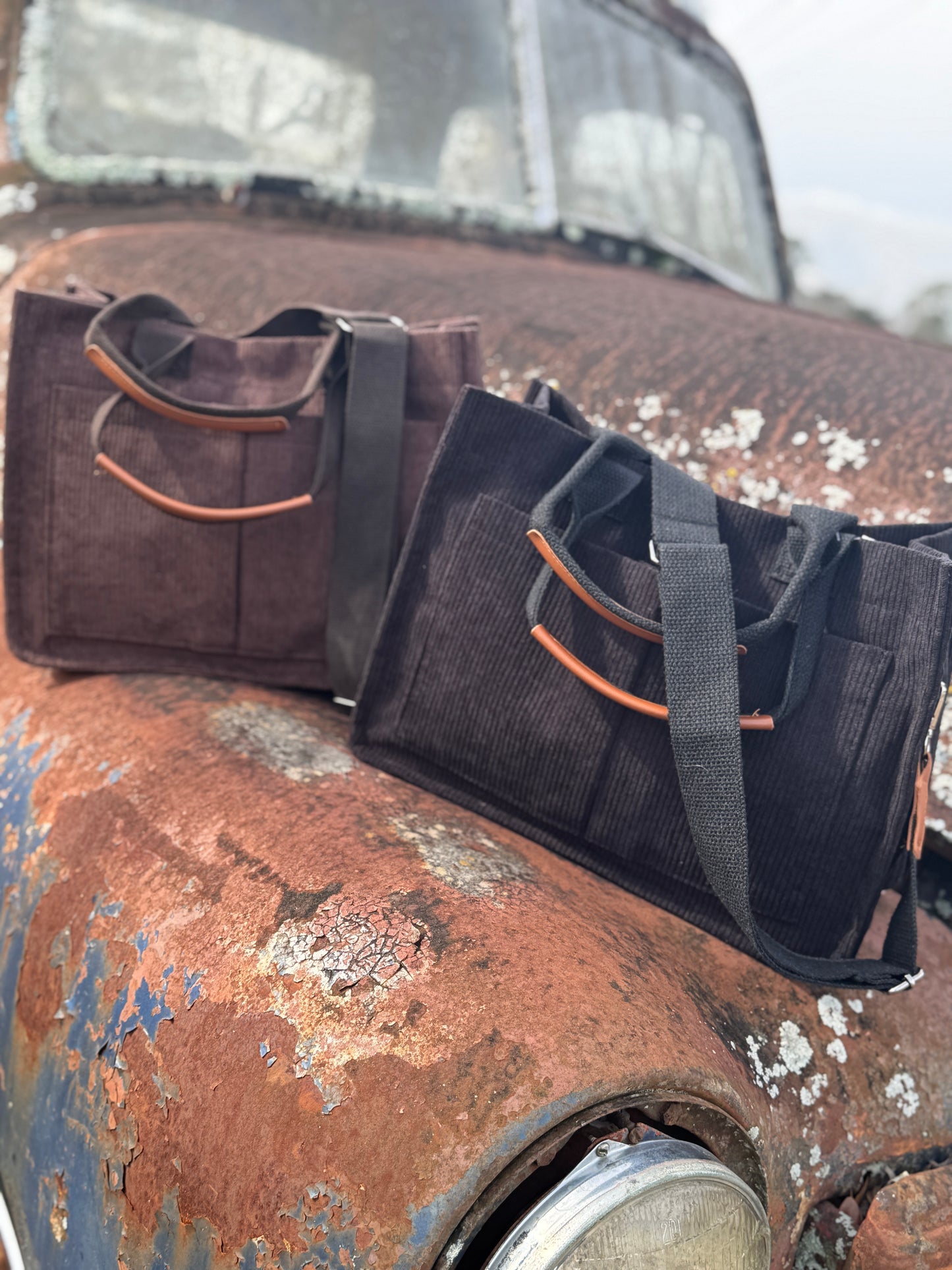 Two bags, one brown and one black with camel accents, on a rusted surface.
