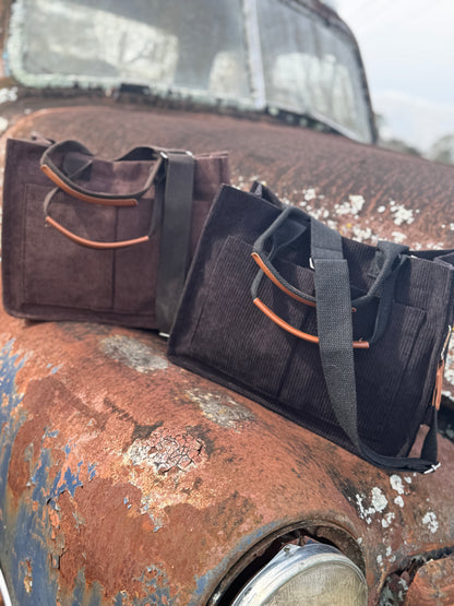 Two bags, one brown and one black with camel accents, on a rusted surface.