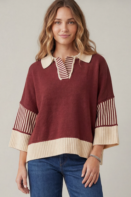 A woman wearing a burgundy knit sweater with cream ribbed trim and striped details on the collar, placket, and three-quarter sleeves, paired with blue jeans against a neutral studio background.