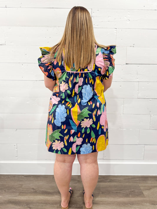 Woman wearing a colorful floral dress against a white brick wall.