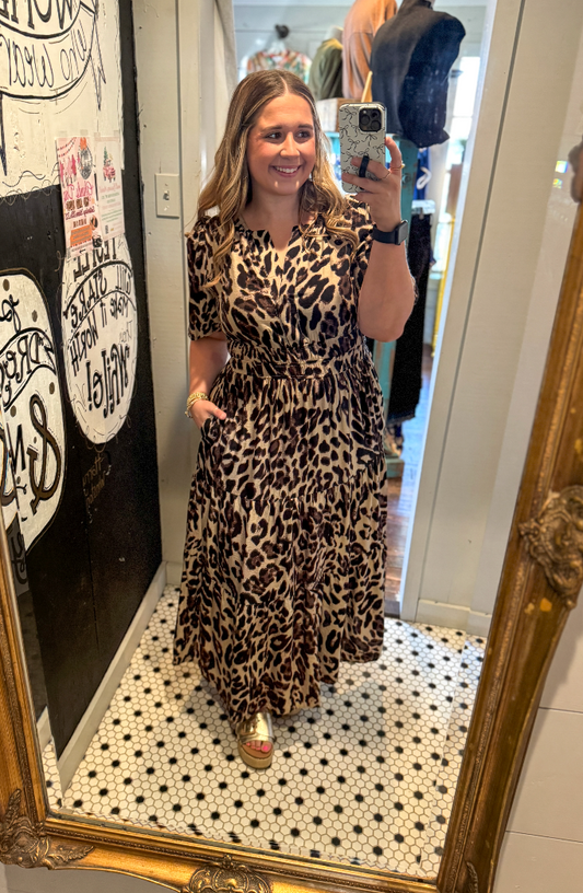 Woman taking a mirror selfie wearing a leopard print dress in a store.