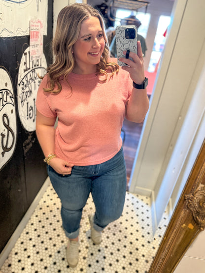 Woman taking a mirror selfie wearing a pink sweater and blue jeans.