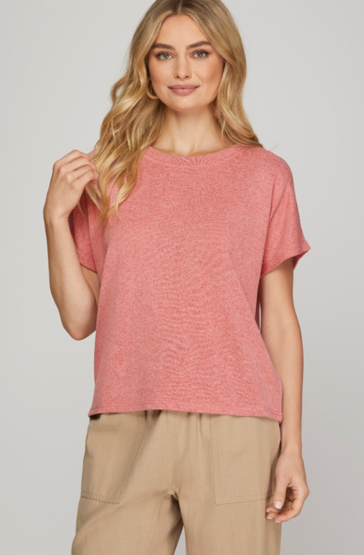 Woman wearing a pink textured top and beige pants on a plain background