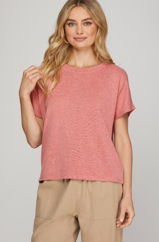 Woman wearing a pink textured top and beige pants on a plain background