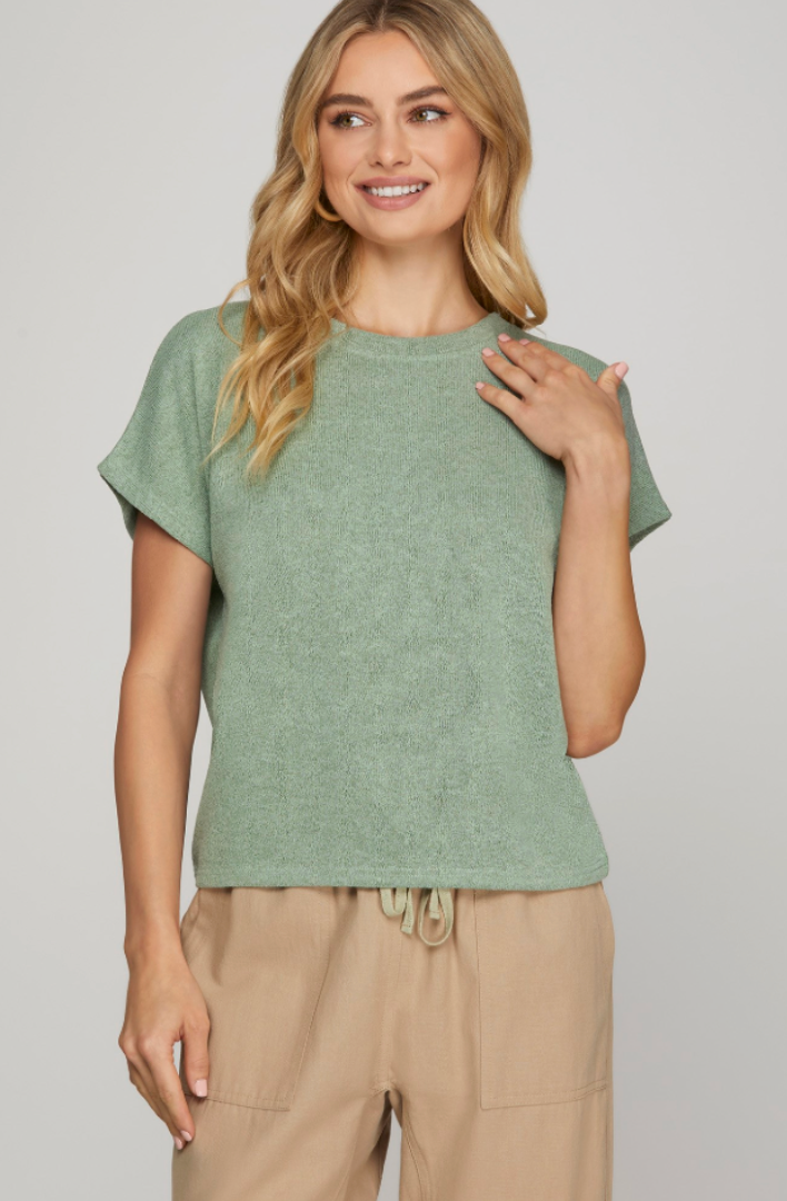 Woman wearing a green top and beige pants against a plain background