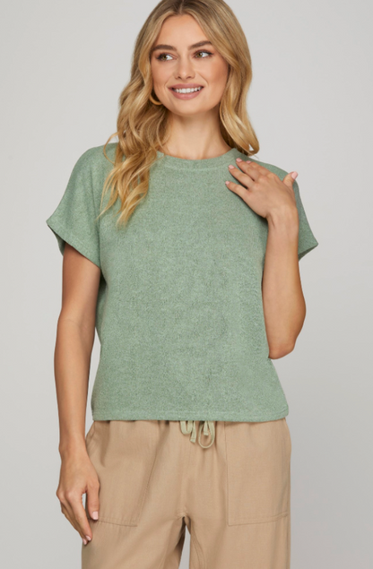 Woman wearing a green top and beige pants against a plain background