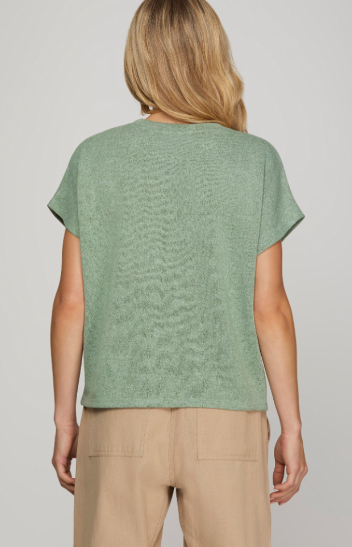 Person wearing a green t-shirt and beige pants on a plain background