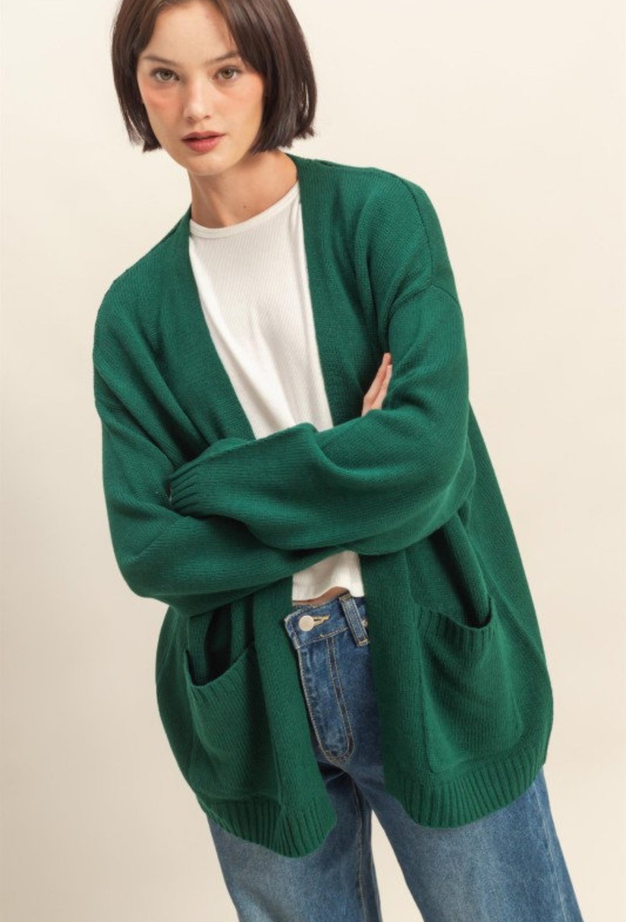 Person wearing a green cardigan over a white shirt and blue jeans on a beige background