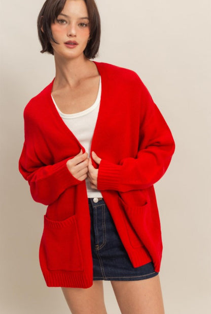 Woman wearing a red cardigan over a white shirt and denim shorts on a beige background