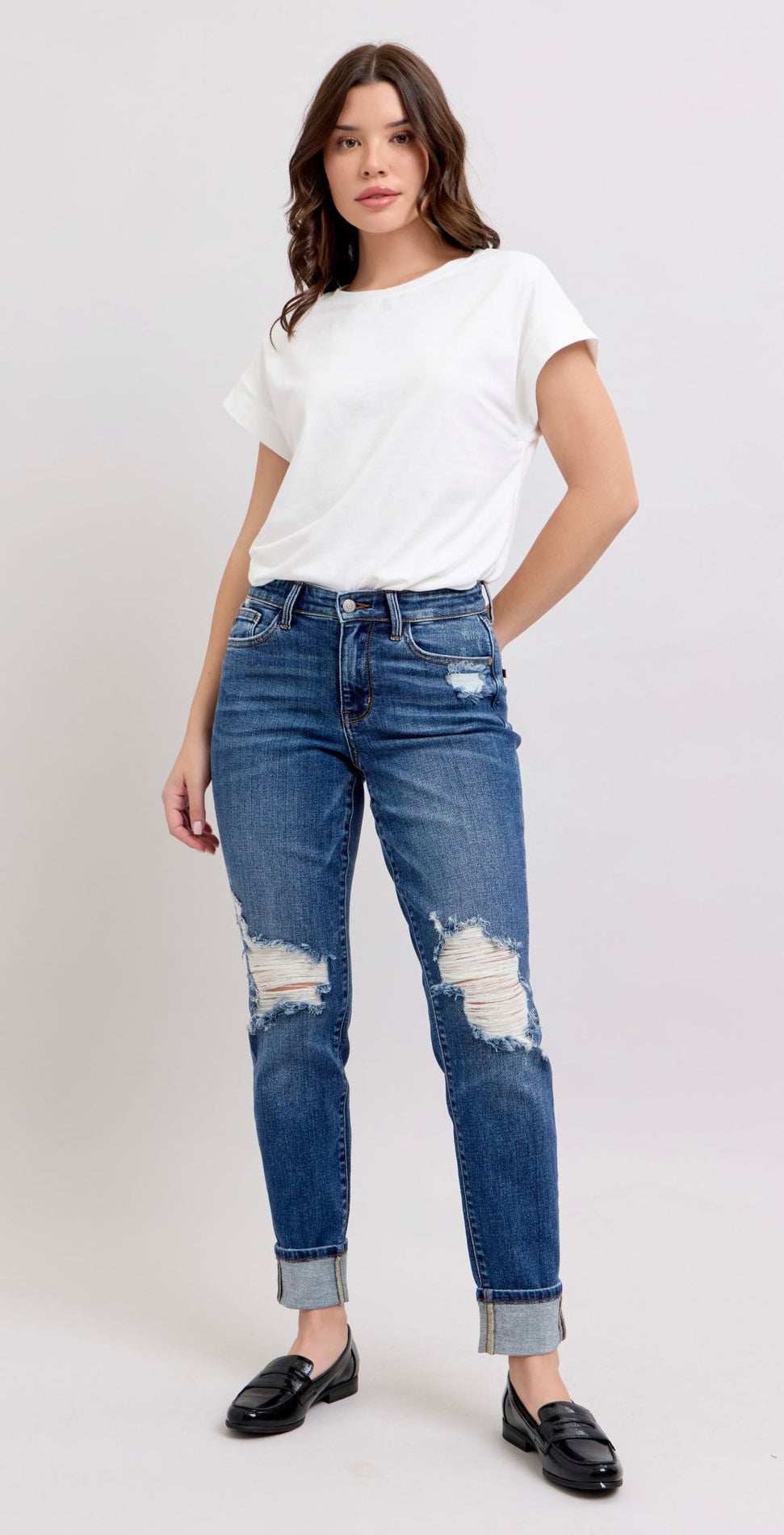 Woman wearing a white t-shirt and blue distressed jeans on a plain background