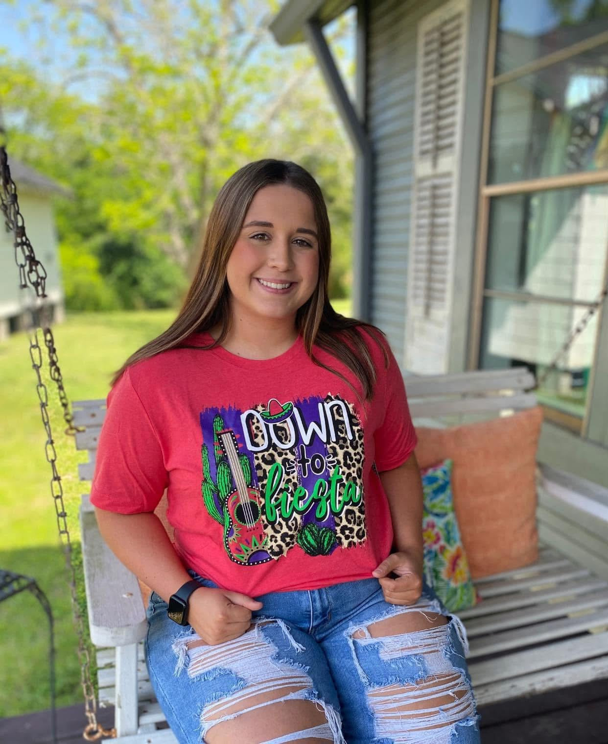Person wearing a red t-shirt with colorful graphics sitting on a porch.
