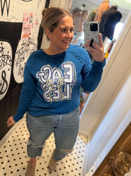 Person wearing a blue sweatshirt with a graphic design, taking a mirror selfie.