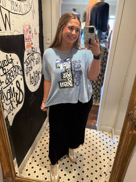 Woman taking a mirror selfie wearing a light blue t-shirt with a graphic design and black pants.