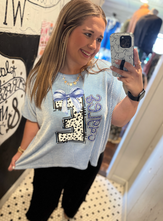 Woman taking a mirror selfie wearing a graphic t-shirt with a large number '25' design.